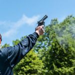 Close-up of a person firing a starting pistol outdoors with blue sky
